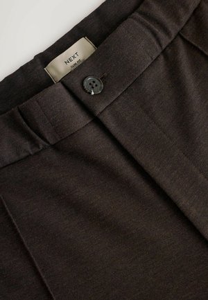 Tamsiai rudos pritaikytos kelnės su vienu mygtuku, raukšlėta priekyje ir etikete "NEXT Slim Fit". Medžiaga yra lygi.