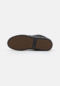 Shoe preto com uma sola de borracha texturizada apresentando um padrão de diamante e um fundo castanho. O sapato também inclui um material superior escuro.