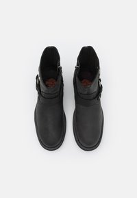 Botines de piel negra con textura suave, puntera redondeada, detalles cosidos y cierre de cremallera lateral con un acento de correa.