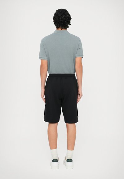 Ανοιχτό γκρι πόλο μπλουζάκι με κοντά μανίκια, συνδυασμένο με μαύρο σορτς. Τα παπούτσια είναι λευκά με πράσινες λεπτομέρειες. Η όψη είναι από πίσω.