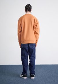 Orange sweatshirt med lange ærmer og rund halsudskæring, parret med mørkeblå cargo-bukser med flere lommer og sorte sneakers.