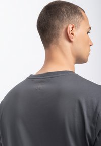 Grijze short-sleeve t-shirt van zachte stof, met een ronde hals en een klein logo gedrukt nabij de achterkant van de halslijn.
