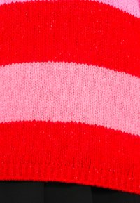 Pull en maille rayé rouge et rose, avec de larges rayures horizontales, une texture douce et un ourlet côtelé.