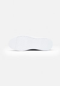 Sole di sneaker bianca con un motivo di texture ondulato. Punta arrotondata e tacco piatto con un branding minimale. Materiale liscio e flessibile.