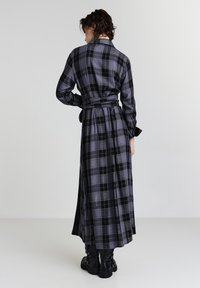 Abito lungo a quadri in nero e grigio, con colletto, cintura in vita e maniche lunghe. Realizzato in tessuto morbido, presenta un design fluido.