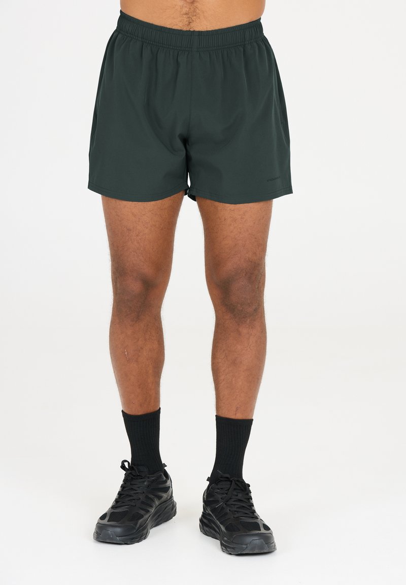 Svarta idrottsshorts med elastisk midja, slät yta och längd ovanför knäna, kombinerade med svarta strumpor och löparskor.