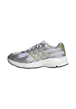 Zapatilla deportiva blanca y plateada con rayas doradas, cordones blancos, parte superior de malla y suela blanca gruesa con dibujo negro visible en un lado.
