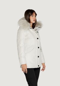 Parka bianca con cappuccio foderato in pelliccia, bottoni neri e due tasche frontali. Tessuto liscio con un design strutturato e cuciture in contrasto.