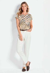 Dierprint blouse in beige en bruin, met korte mouwen en knoopdetails; gecombineerd met witte broek en donkere geweven instappers.
