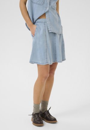 Gonna di jeans azzurri chiari con forma svasata, cuciture a contrasto e tasche frontali, indossata con scarpe scure con lacci e calzini grigi.