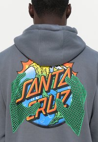 Felpa grigia con cappuccio che presenta un grafico colorato sul retro con la scritta "SANTA CRUZ", circondata da mani verdi e un design di un globo.
