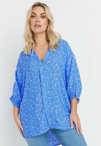 Blusa floreale blu con scollatura a V, maniche a tre quarti e polsini arricciati; tessuto leggero con delicati motivi di fiori bianchi e gialli.