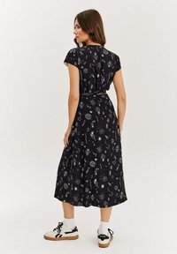 Černé šaty s bílými vzory hvězd, srdcí a symbolů. Střední délka, s krátkými rukávy a detailem uvázaného pasu, doplněné teniskami.