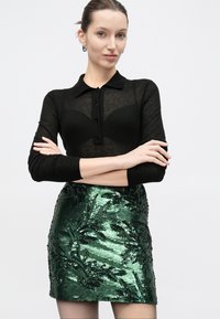 Μαύρο, μακρυμάνικο πουκάμισο με κουμπιά και διαφανή υφή, συνδυασμένο με εφαρμοστή, πράσινη μίνι φούστα με παγιέτες και σχέδια φύλλων.