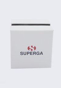 Bela kvadratna škatla z teksturirano površino, na sprednji strani z rdečim logotipom "S" in "SUPERGA" v črni pisavi, zasnovana za pakiranje.