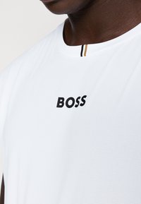 Λευκό μπλουζάκι κοντομάνικο με υφή. Διαθέτει μαύρο λογότυπο "BOSS" και γιακά με μαύρες και χρυσές ρίγες.