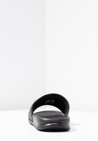 Svart öppen tå-sandal med texturerat fotbädd och bred rem, visad från en låg frontal vinkel på en vit yta.