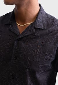 Short-sleeve black shirt featuring intricate embroidery with floral and geometric patterns, made from lightweight fabric, with a button-down front.