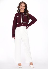 Chaqueta corta burdeos con ribete y botones blancos, combinada con pantalones de pierna ancha blancos de cintura alta y tacones blancos a juego.