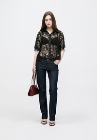 Black lace blouse with short sleeves, button front, paired with dark blue denim jeans. Holds a small red handbag and wears black sandals.