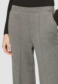 Graue, schmal zulaufende Hosen aus weichem, strukturiertem Stoff. Sie verfügen über einen breiten Bund, seitliche Taschen und dezente Falten für einen eleganten Look.