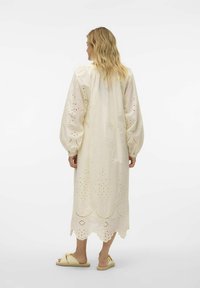 Lång, krämfärgad klänning i bomull med broderie anglaise-detaljer, puffärmar och scalloped nederdel; bärs med platta sandaler.