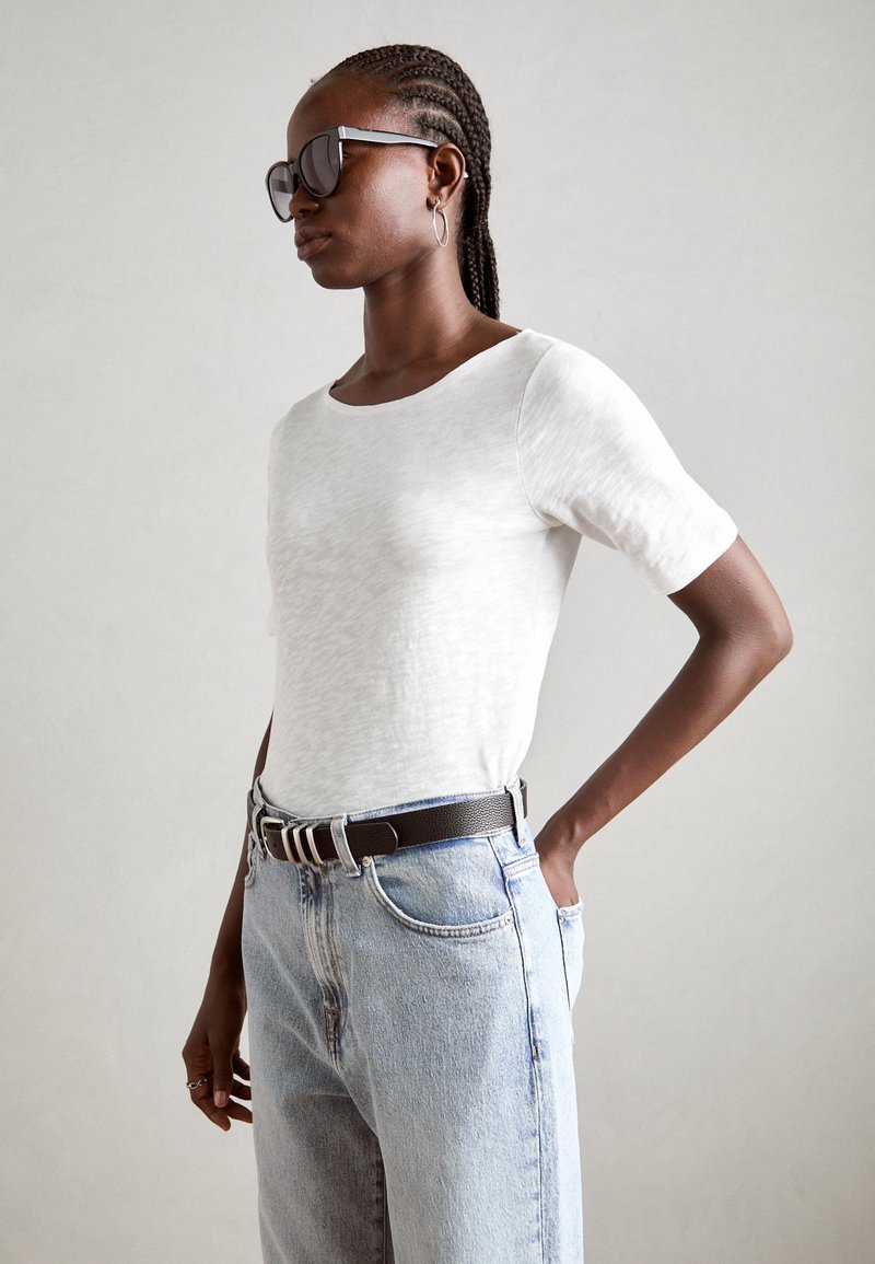 White short-sleeve T-shirt with a smooth texture, paired with light blue high-waisted jeans and a black belt featuring silver hardware.