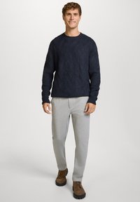 Navy gebreide trui met een textuurpatroon in chevron, lichtgrijze joggingbroek en bruine veterschoenen. Een eenvoudige en casual outfit.