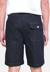 Shorts in denim blu navy con cintura elasticizzata, tasca posteriore con chiusura a scatto e dettaglio con orlo arrotolato. La texture è robusta e liscia.