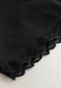 Fekete szövet fogazott csipke szegéllyel az élén, részletes mintákkal és sima textúrával.