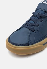 Navy zili sneakers ar gludu ādas virsu, teksturētām akcentiem un gumijas zoli, ar apaļu purngalu un auklām priekšpusē.
