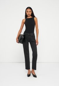 Body a costine nera abbinato a jeans neri a vita alta, una pochette in pelle nera e décolleté neri a punta, su uno sfondo bianco.