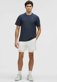 Camisa atlética de manga corta en color marino combinada con pantalones cortos blancos. La camisa tiene un cuello redondo y un logo sutil; los pantalones cortos presentan un diseño texturizado.