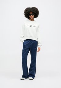 Svetrová mikina s okrúhlym výstrihom v svetlo sivej farbe s logom "NIKE SHOX", spojená s námornícky modrými teplákmi s bielymi bočnými pásmi a čiernymi teniskami.