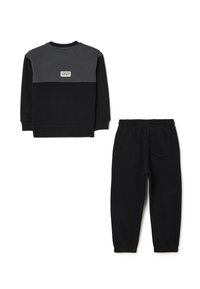 Felpa nera e grigia con colletto tondo e un piccolo patch; abbinata a pantaloni della tuta neri con vita elastica e tasca laterale.