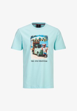 T-shirt bleu clair avec un graphisme d'un ours portant des lunettes de soleil et des vêtements de plage, appuyé contre un petit chariot de plage vert sous un auvent à rayures.
