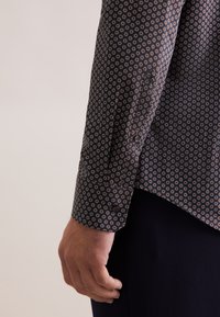 Zwart overhemd met een klein cirkelpatroon in wit, rood en blauw. Met een knoopmanchet en een gebogen zoom.
