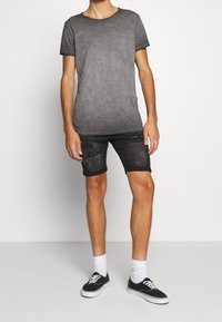 T-shirt gris dégradé à manches courtes, associée à un short en denim foncé vieilli et des baskets noires avec des semelles blanches et des chaussettes blanches.