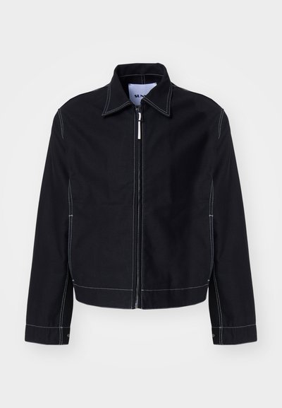 Schwarze Denimjacke mit einem kurzen Design, weißen Nähten, einem spitzen Kragen und einem Reißverschluss vorne. Lange Ärmel mit geknöpften Manschetten.