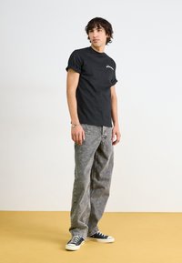 Camiseta de algodón negra con mangas enrolladas y logo blanco en el pecho, combinada con jeans holgados grises y zapatillas negras con suelas blancas.