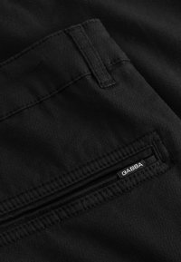 Fekete szövetnadrág cipzáras zsebbel és egy kis márkacímkével. A szövet sima, puha tapintású.