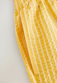 Tissu jaune à rayures blanches verticales, avec un gros plan sur une ceinture élastique et une couture latérale avec surpiqûres.