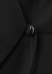 Gros plan sur un tissu noir avec un anneau métallique argenté tenant une sangle noire en place, probablement une partie d’un vêtement ou accessoire.