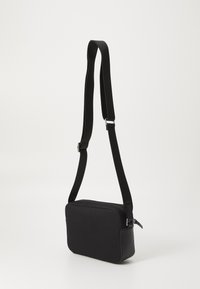 Borsa a tracolla nera in tessuto con spallaccio regolabile, forma rettangolare, chiusura con zip, texture sottile e accenti in metallo.