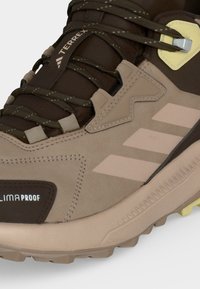 Καφέ και μπεζ πεζοπορικό παπούτσι Adidas Terrex με αντανακλαστικά κορδόνια, ετικέτα Climaproof και χοντρή ανθεκτική σόλα για χρήση σε εξωτερικούς χώρους.
