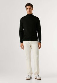 Maglione nero a collo alto con design aderente, abbinato a pantaloni dritti color crema e sneakers bianche con dettagli neri.