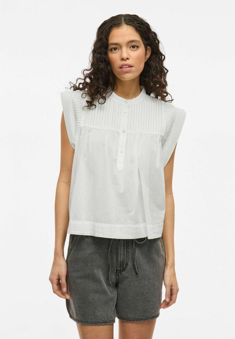 Witte blouse met korte mouwen en geribbelde structuur op de schouders, knopen aan de voorkant en een losse pasvorm. Gemaakt in combinatie met grijze shorts met trekkoord.