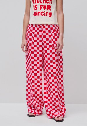 Personne portant un pantalon évasé à motif damier rouge et blanc et un haut blanc sans manches avec l'inscription « la cuisine c'est POUR danser. »