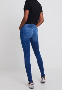 Smala jeans i mörkblå denim med en slät yta, som har bakfickor och en midjehöjd på normal nivå. Kombinerat med en svart t-shirt och sneakers.