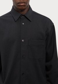 Zwarte button-up shirt met een gestructureerde kraag, een klein borstzakje en een subtiele textuur. Bevat bijpassende knopen en een getailleerde pasvorm.